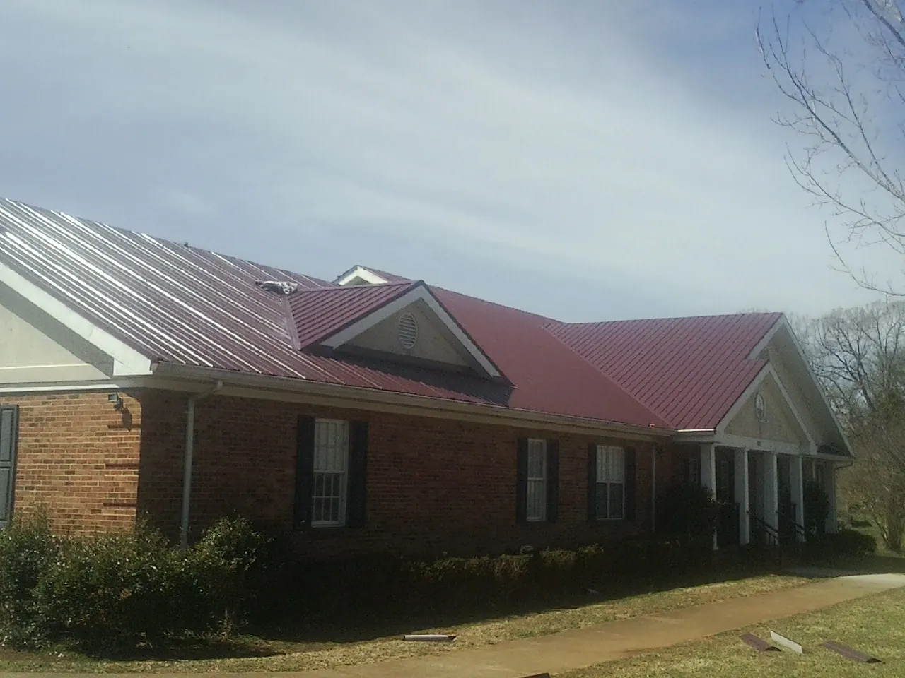 Red metal roof with gabled entries on a long brick building, from a Hail Damage Roof Repair job in Knotts Island