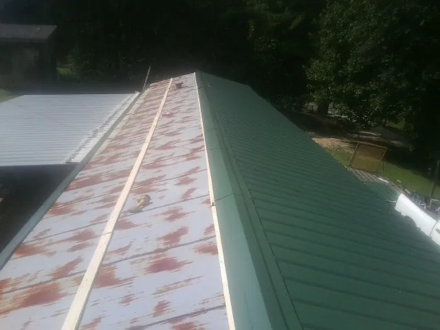 Old rusted panels beside newly installed green metal roofing — Wind Damage Roof Repair by Roofing Brothers in Knotts Island