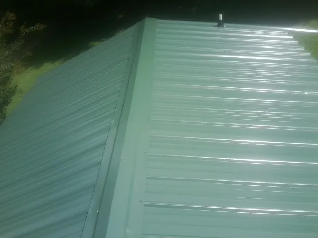New green metal panels meeting at the ridge of a roof — Flat Roof Repair work by our crew in Knotts Island