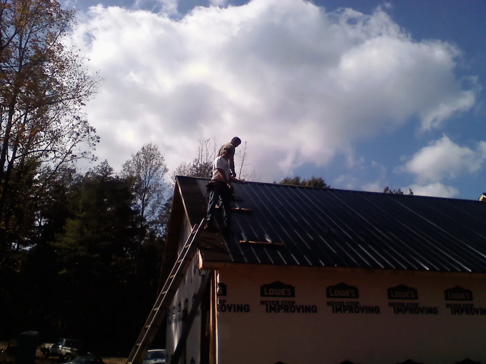 Roofer fastening dark metal panels high against a cloudy sky, from a Roof Inspection job in Knotts Island