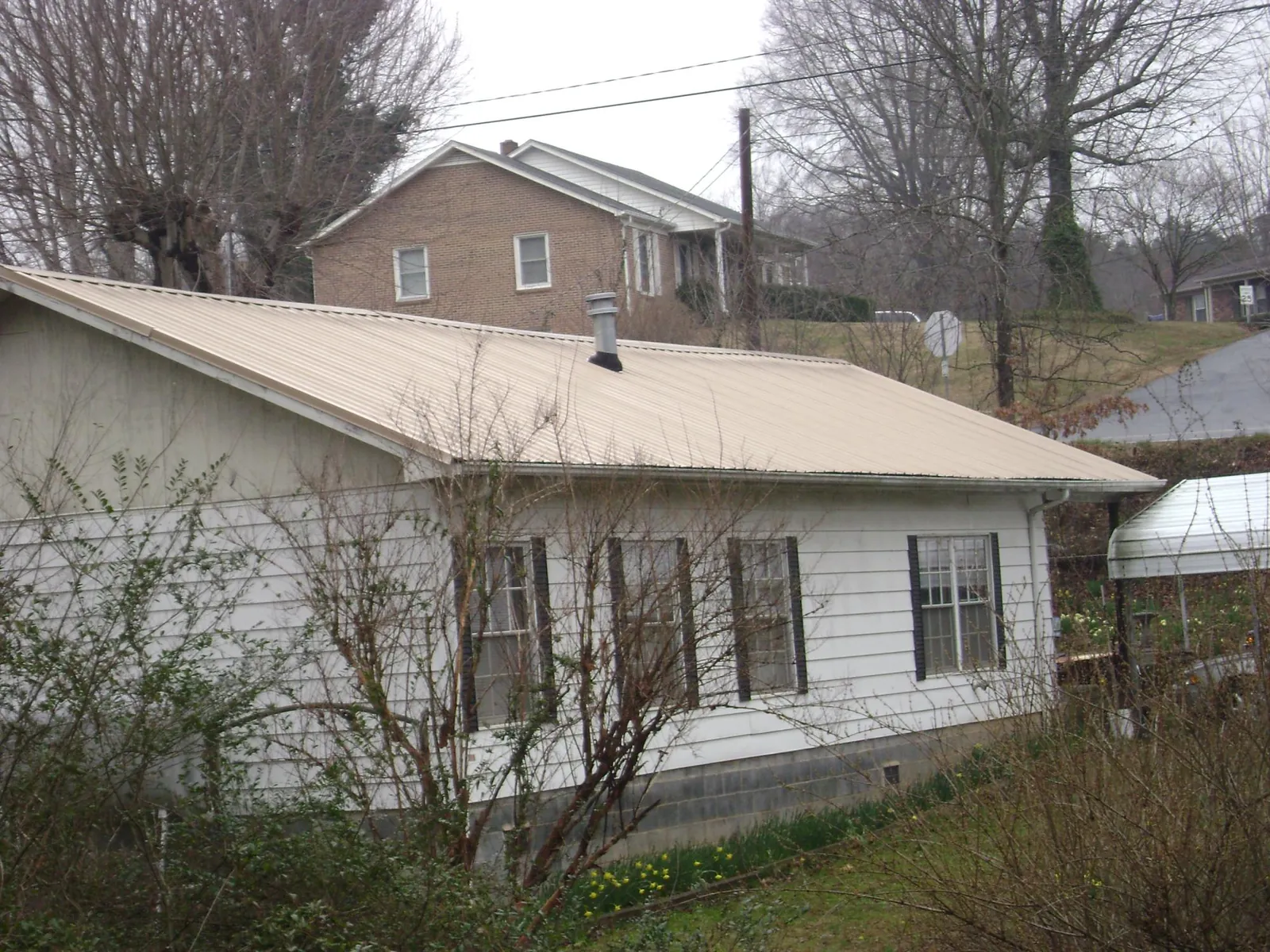 Tan metal roof on a white sided house set into a hillside — Commercial Roofing by Roofing Brothers in Knotts Island