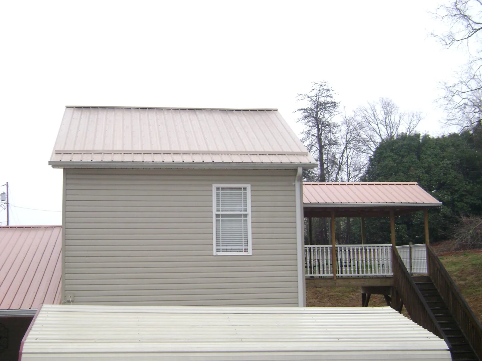 Tan metal roofs on a two story addition and attached porch, from a Roof Replacement job in Knotts Island